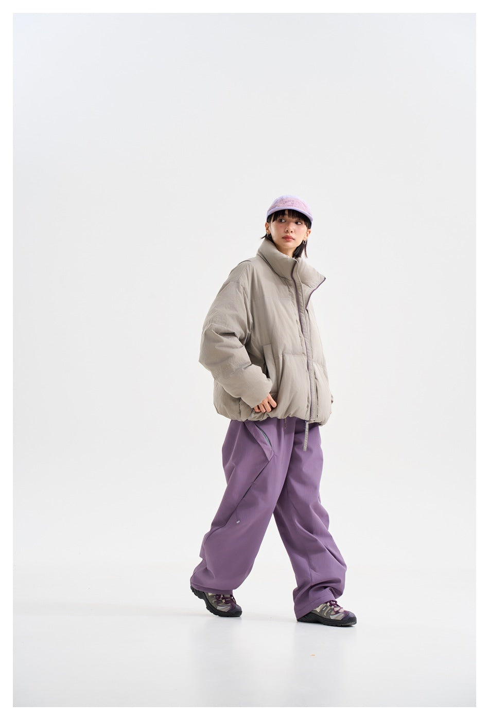 Model in a light gray puffer jacket and loose purple trousers, shown in a walking three-quarter pose.