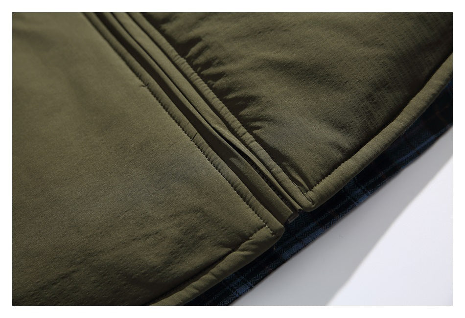 Close-up of the front zipper, lower hem, and dark plaid lining of an olive green jacket.