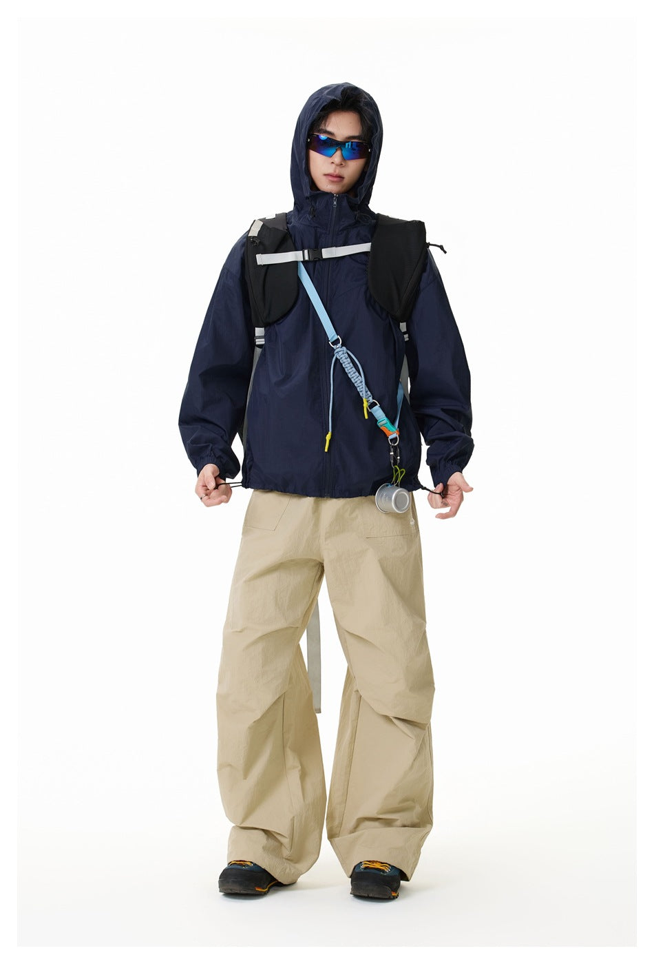Model in navy hooded zip jacket with hood up, wide khaki pants and backpack, full-length view
