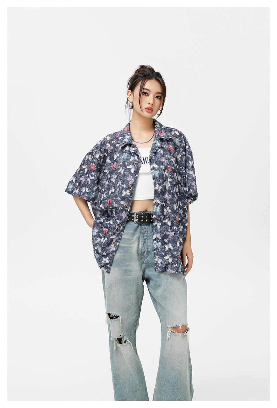 Closer front view of a model wearing a navy butterfly-print short-sleeve button-up shirt and ripped light-wash jeans.