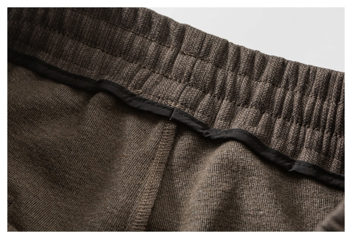 Inside close-up of dark brown trousers showing a gathered waistband, seam, and black binding.