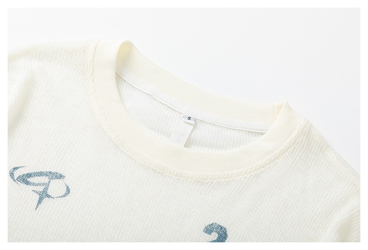 Close-up of an ivory knit shirt neckline with a small size tag and partial blue chest print.