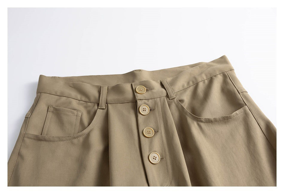 Close-up of taupe trousers showing the waistband, front pockets, belt loops, and four-button fly.