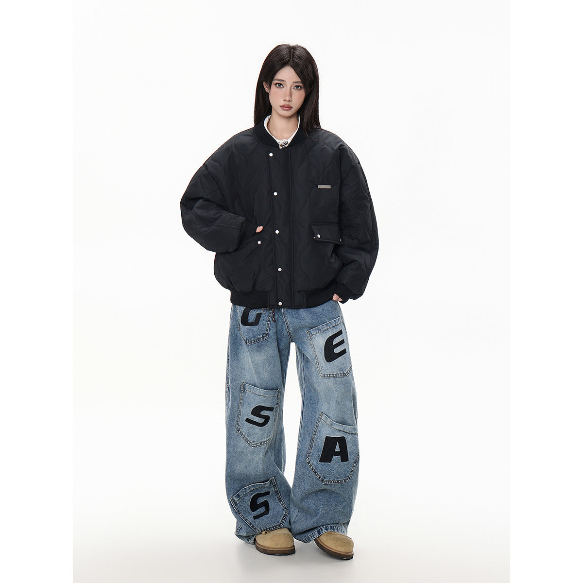 Model wearing a black quilted snap-front bomber jacket with ribbed cuffs and hem, styled with oversized lettered jeans.