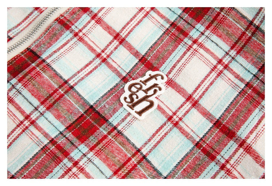 Close-up of a small brown-and-white embroidered patch on red, cream, and pale blue plaid fabric.