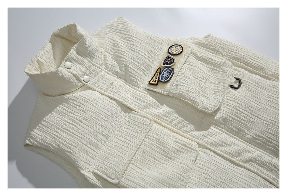Angled view of an ivory vest laid flat, showing its high collar, snap front, two flap pockets, and decorative badges.