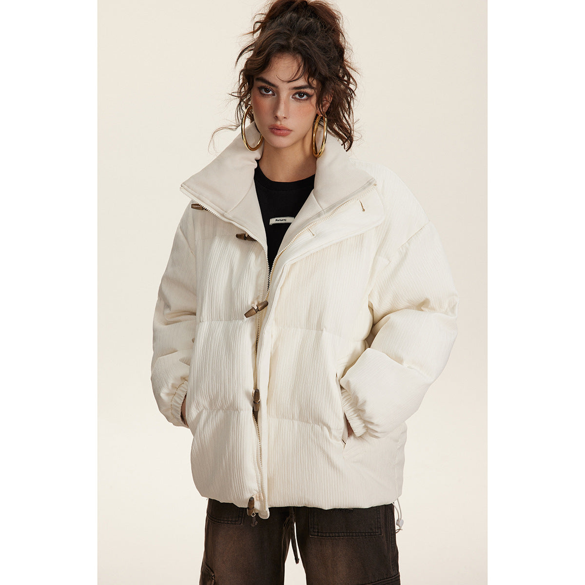 Model wearing an ivory padded jacket with a high collar, zipper and wooden toggle closures.