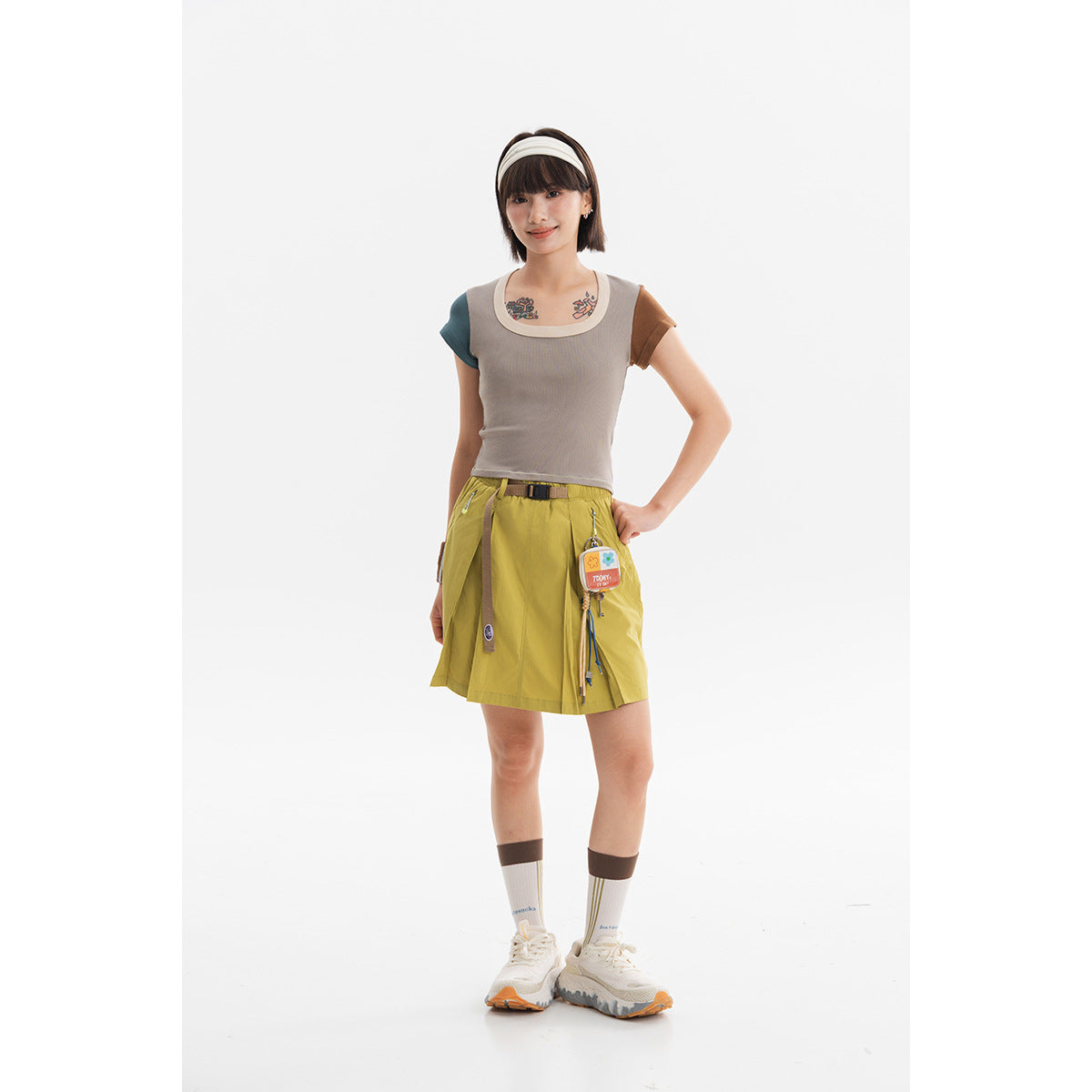 Model wearing a taupe color-block scoop-neck top and mustard utility shorts with a belt and hanging accessories.