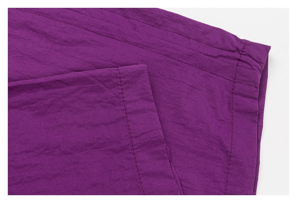 Close-up of purple pants showing stitched panel seams and a folded, topstitched edge.