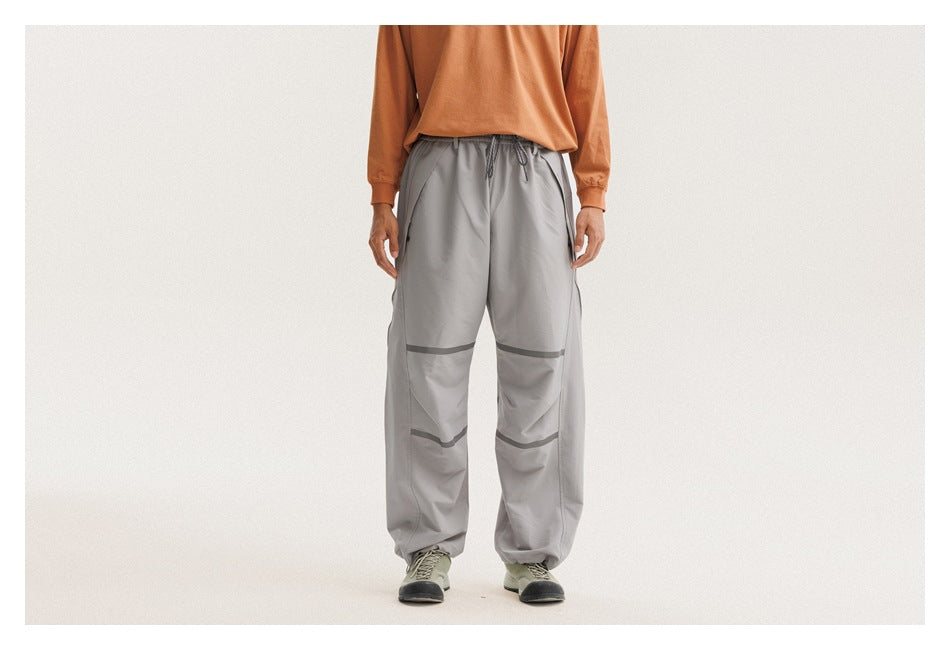Front view of a person wearing loose gray drawstring pants with dark bands across the knees and lower legs.
