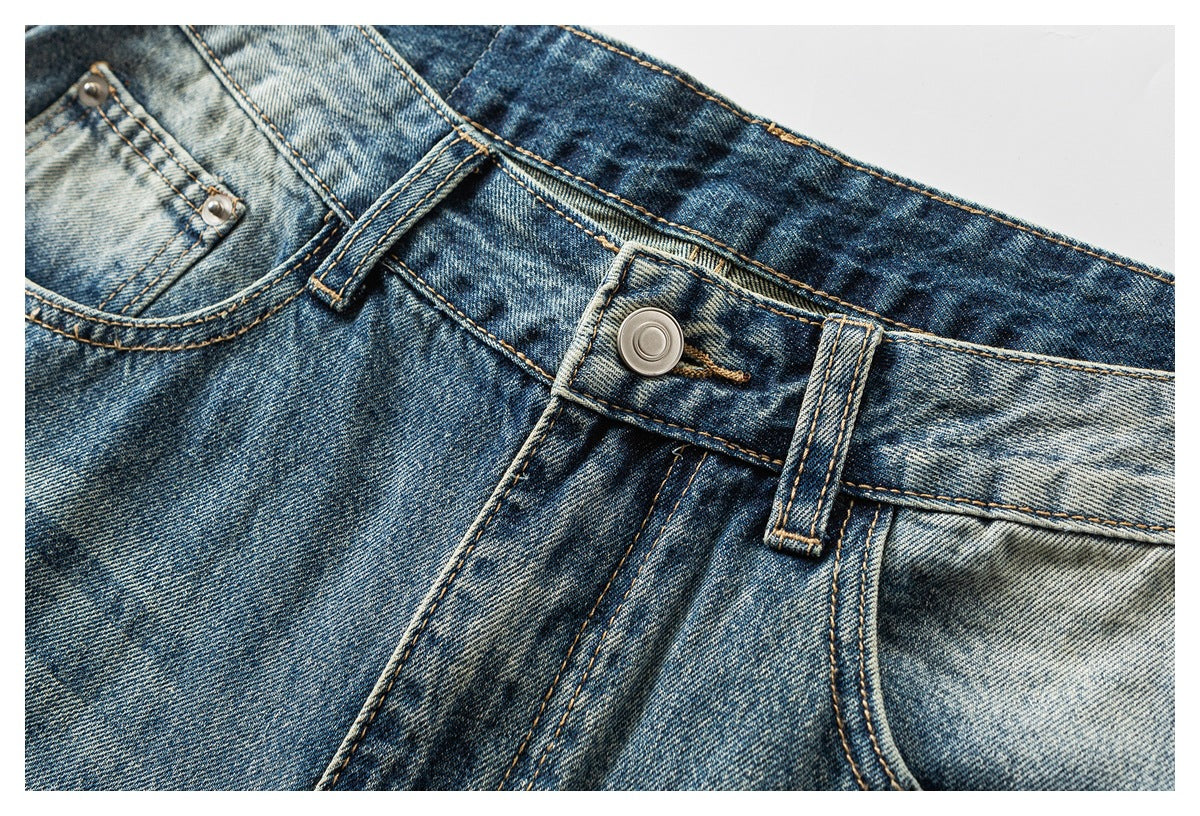 Close-up of faded blue jeans showing the front waistband button, belt loops, fly stitching, and coin pocket.