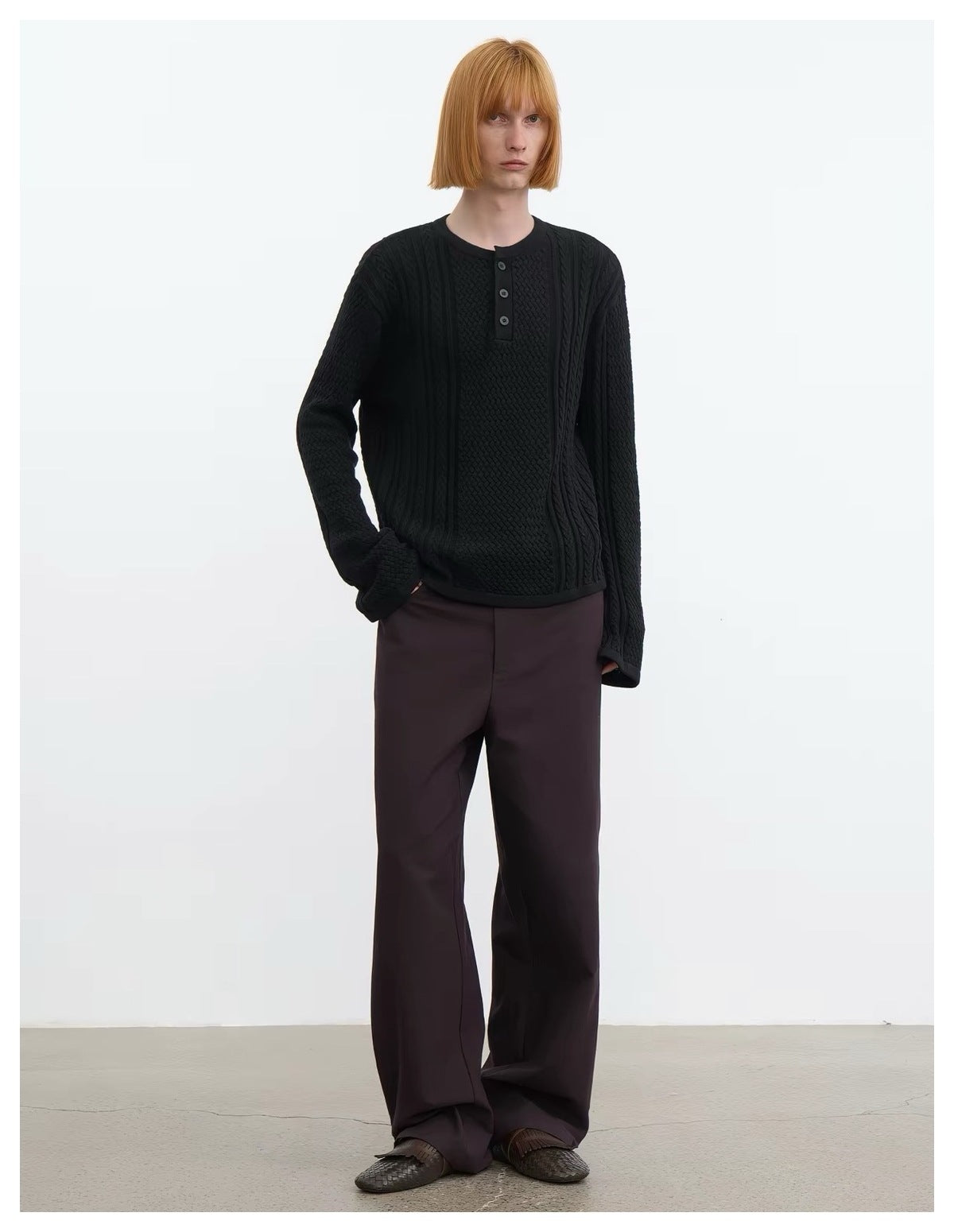 Model wearing black cable-knit Henley sweater with dark brown wide-leg trousers, standing full length