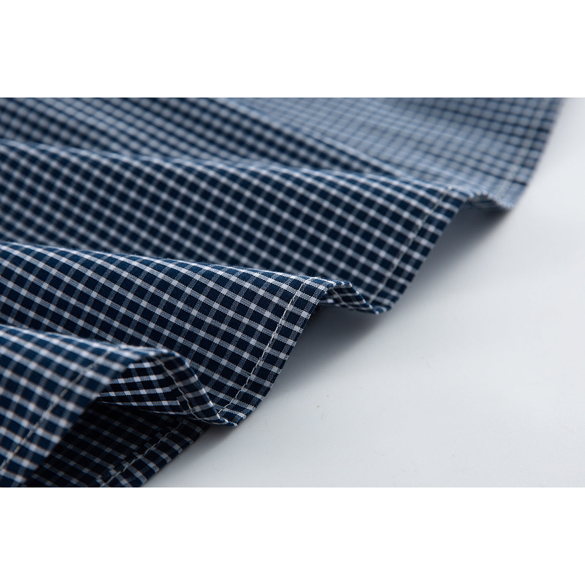Close-up of navy-and-white gingham shirt fabric showing folded seams and stitching.