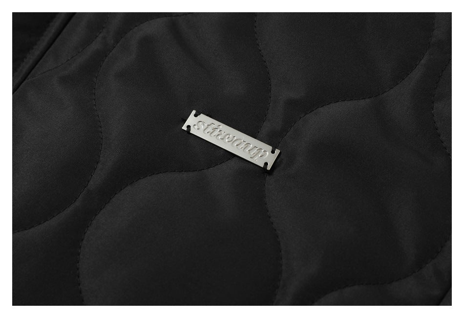 Close-up of a small metal brand plate on the black jacket’s quilted fabric.