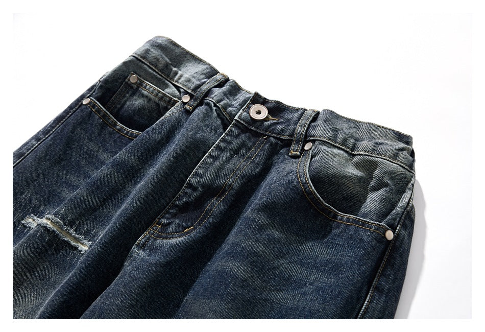 Cropped front view of dark washed blue jeans with a button waist, front pockets and a distressed thigh detail.