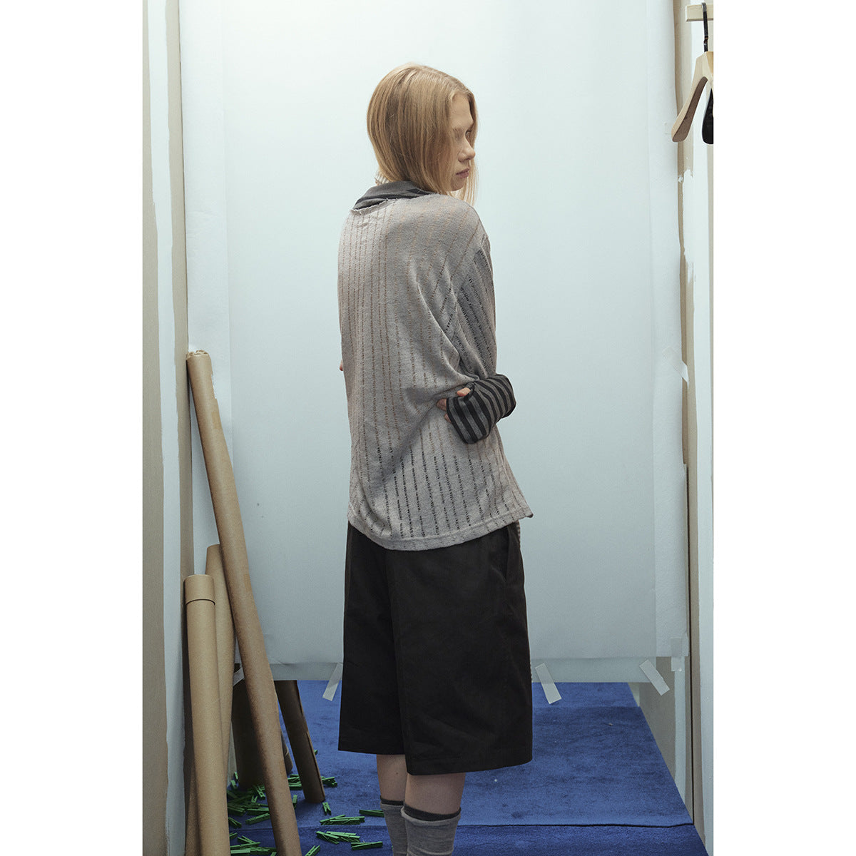 Rear view of a model wearing a gray striped top with dark cuffs and black knee-length shorts.