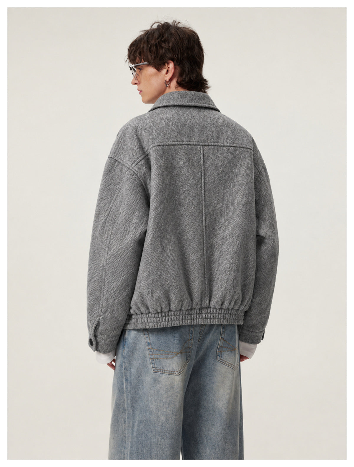 Back view of man wearing gray textured cropped jacket with elastic hem and light-wash wide-leg jeans