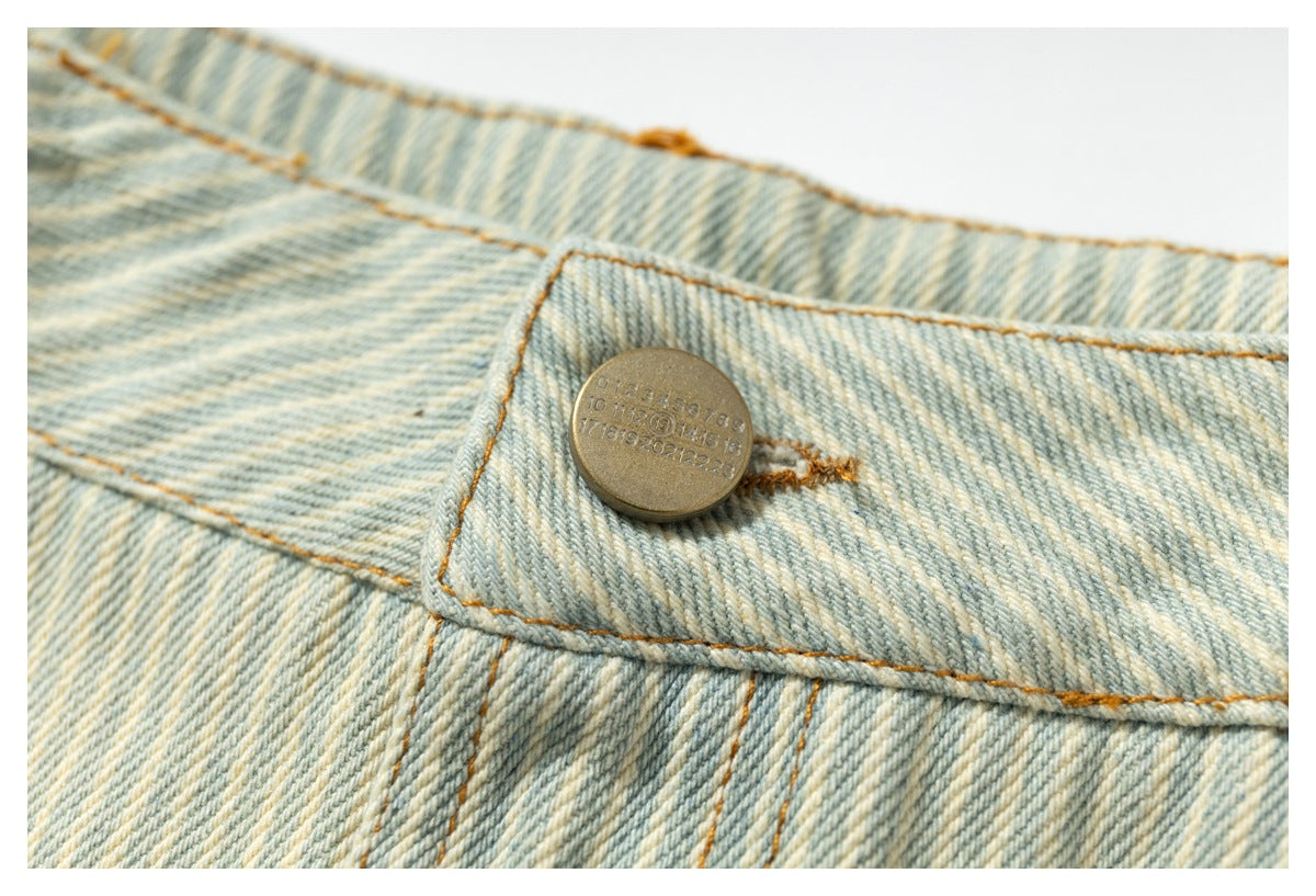 Close-up of the metal button and orange stitching on pale blue striped shorts.