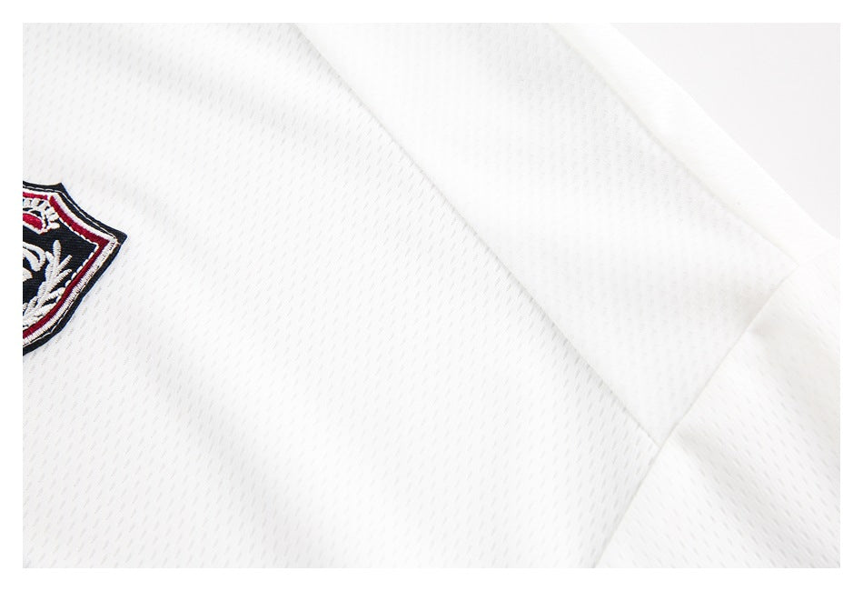 Close-up of a white jersey's perforated fabric, shoulder seam, and embroidered shield crest.