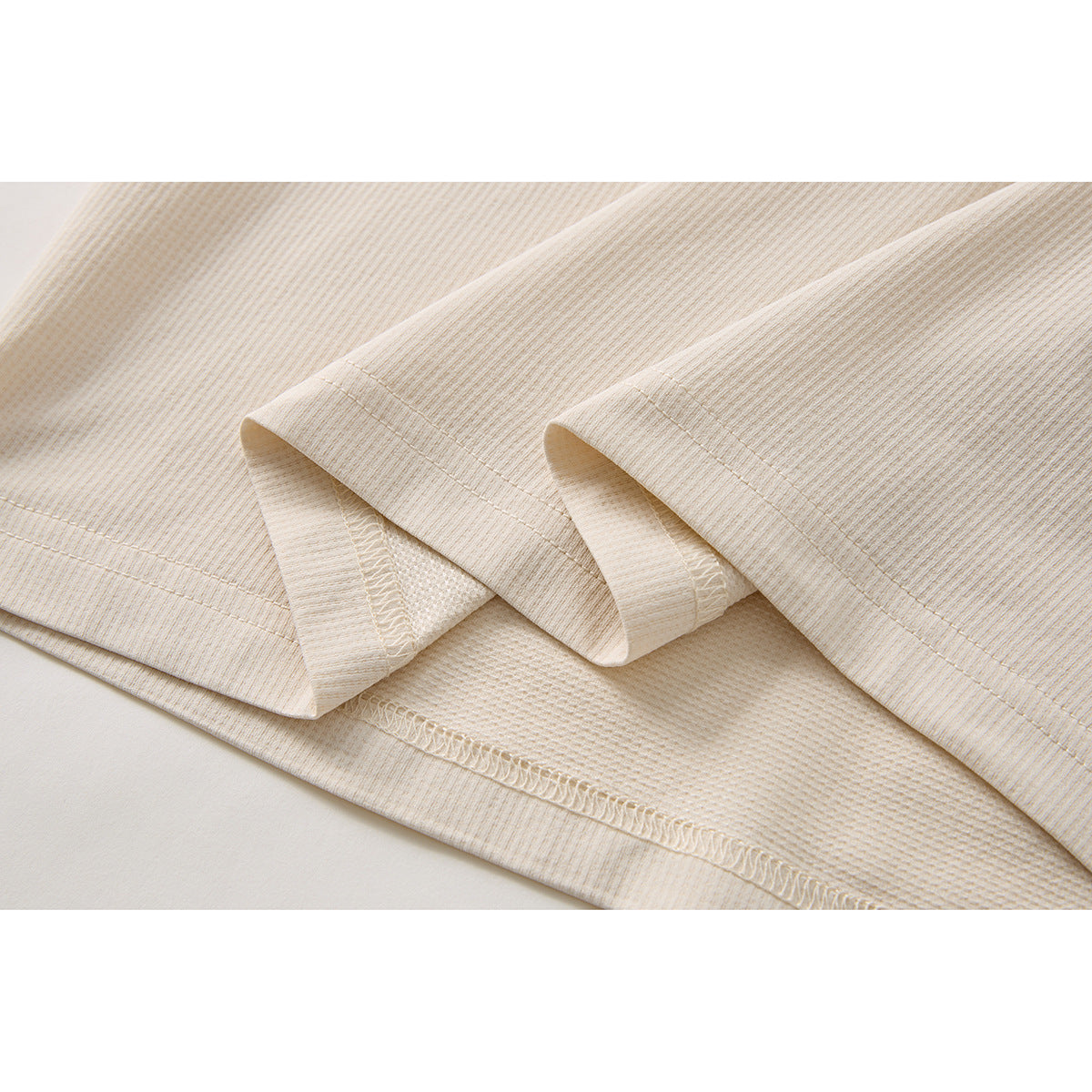 Close-up of the ivory shirt’s folded hem, showing stitching and the textured knit fabric.