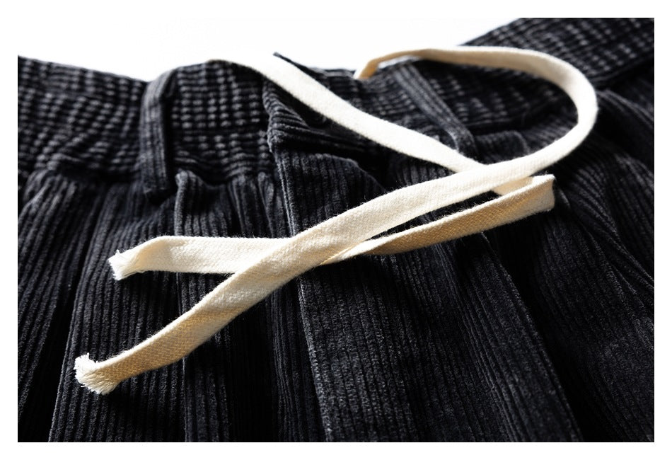 Close-up of black ribbed trousers with cream drawstrings resting across the waistband.