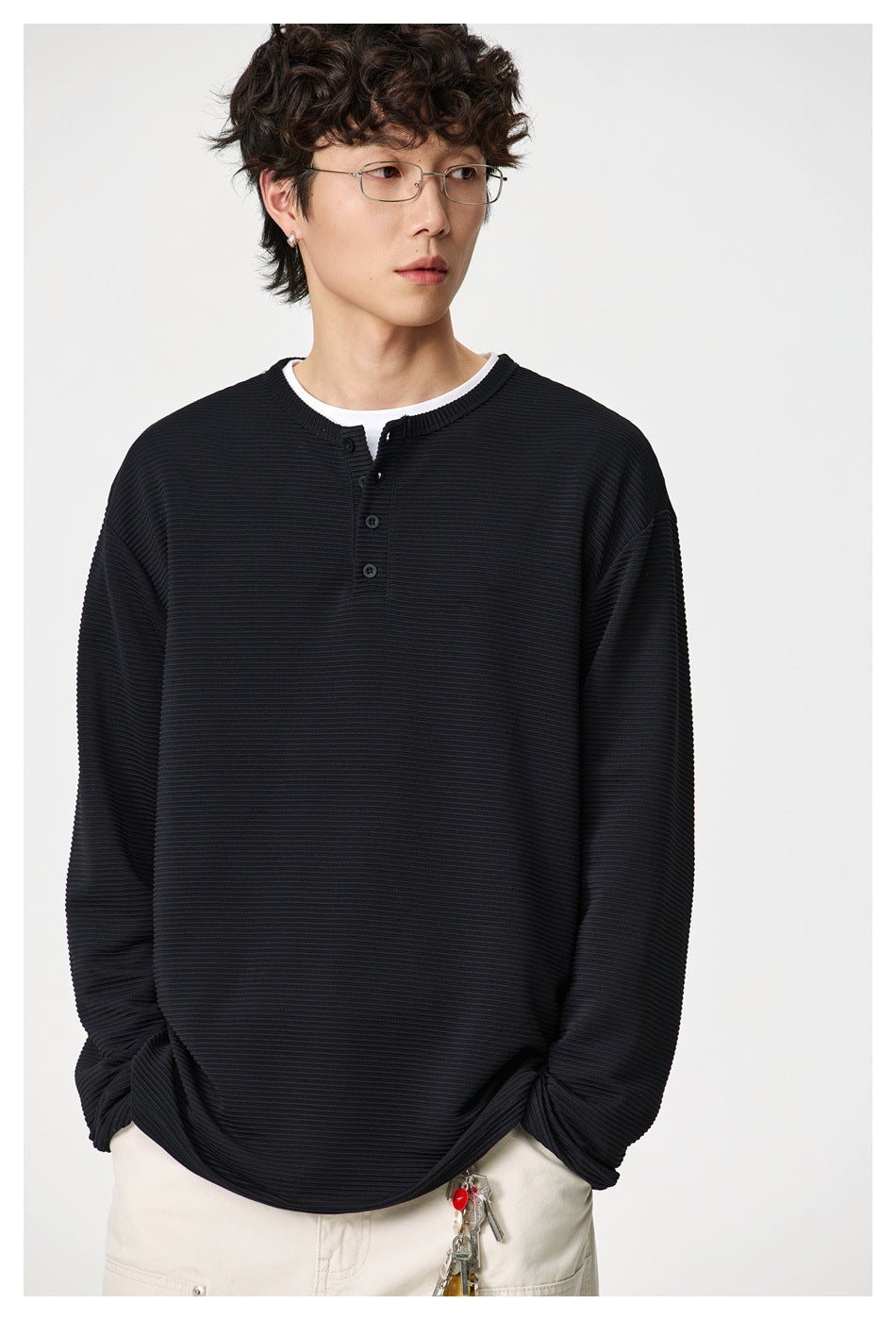 Close view of a model wearing a black ribbed henley with a short button placket and cream trousers.