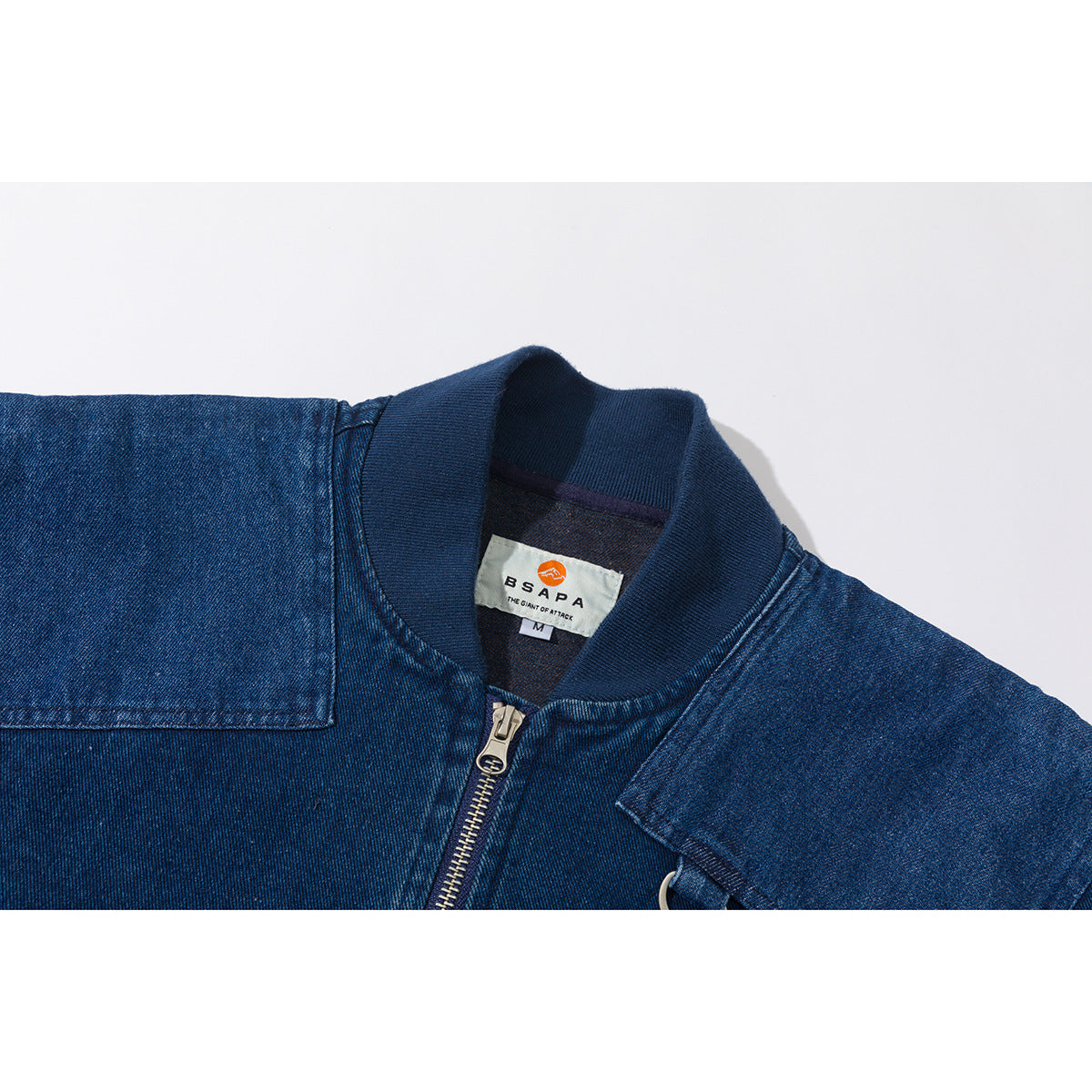 Close-up of a blue denim jacket collar, front zipper, shoulder panels, and sewn neck label.