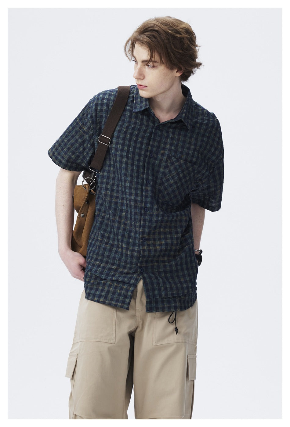 Close-up of model wearing dark check short-sleeve shirt with a brown shoulder strap and beige cargo pants