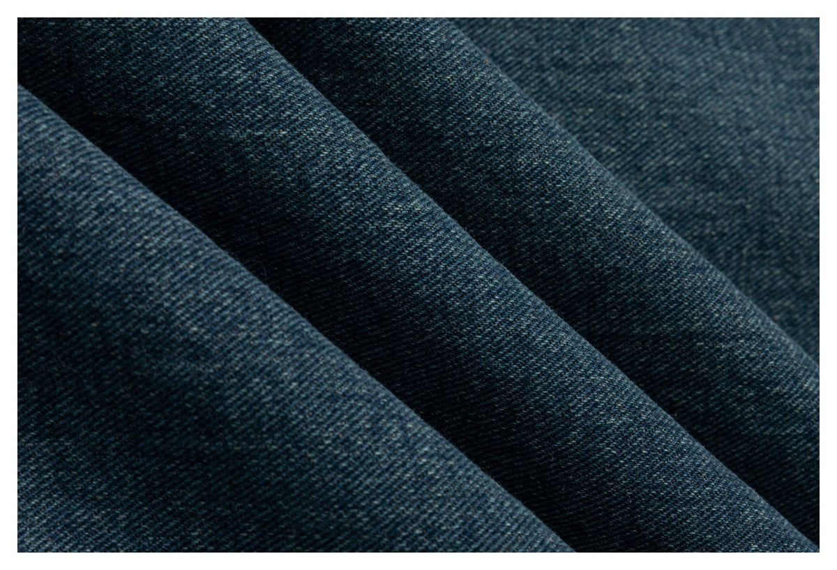 Close-up of dark blue denim fabric folded into ridges, showing its diagonal woven texture.