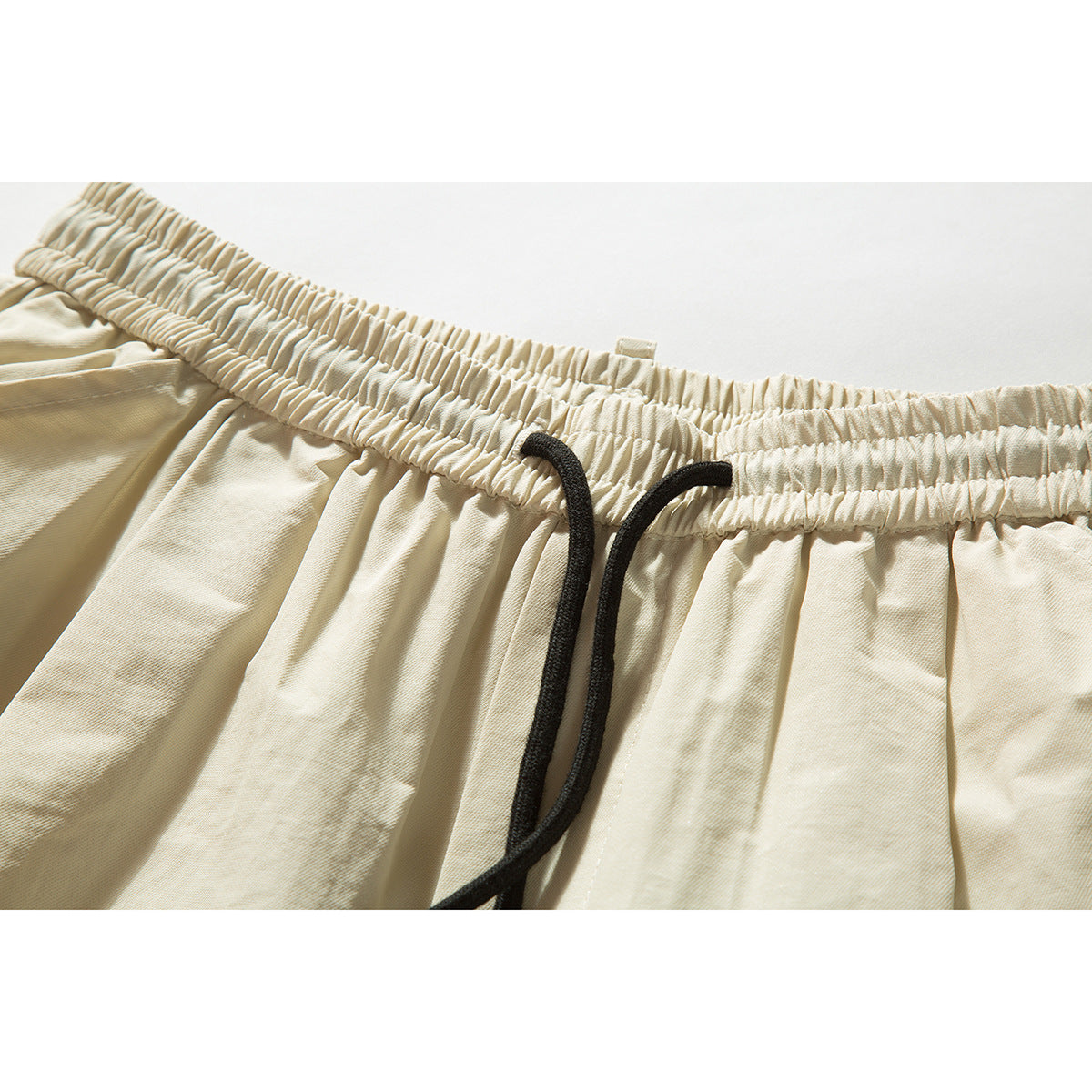 Close-up of cream shorts with a gathered elastic waistband and black drawstring.