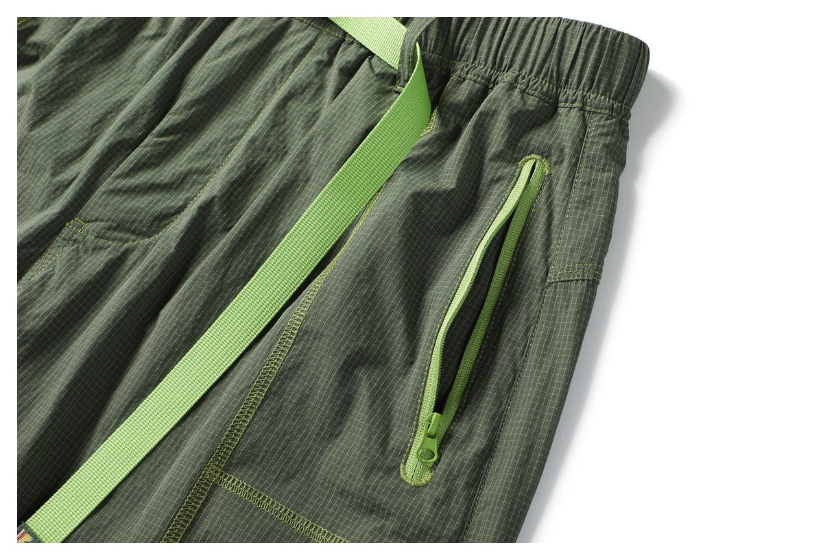 Close-up of an olive check-pattern pant leg with a lime-green zip pocket and belt strap.