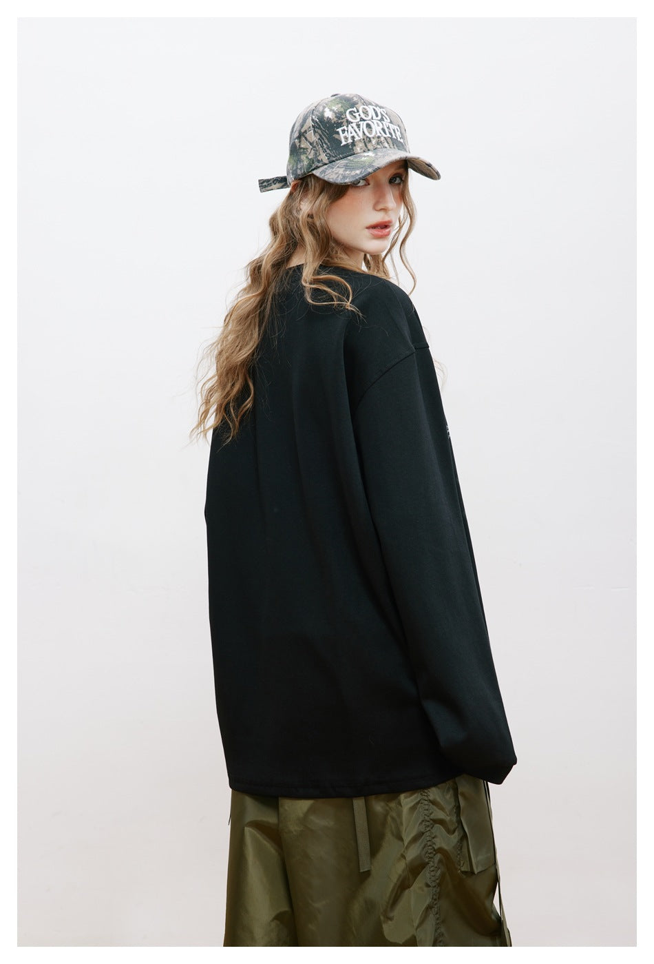Rear view of a model wearing a plain black oversized long-sleeve top and olive cargo pants.