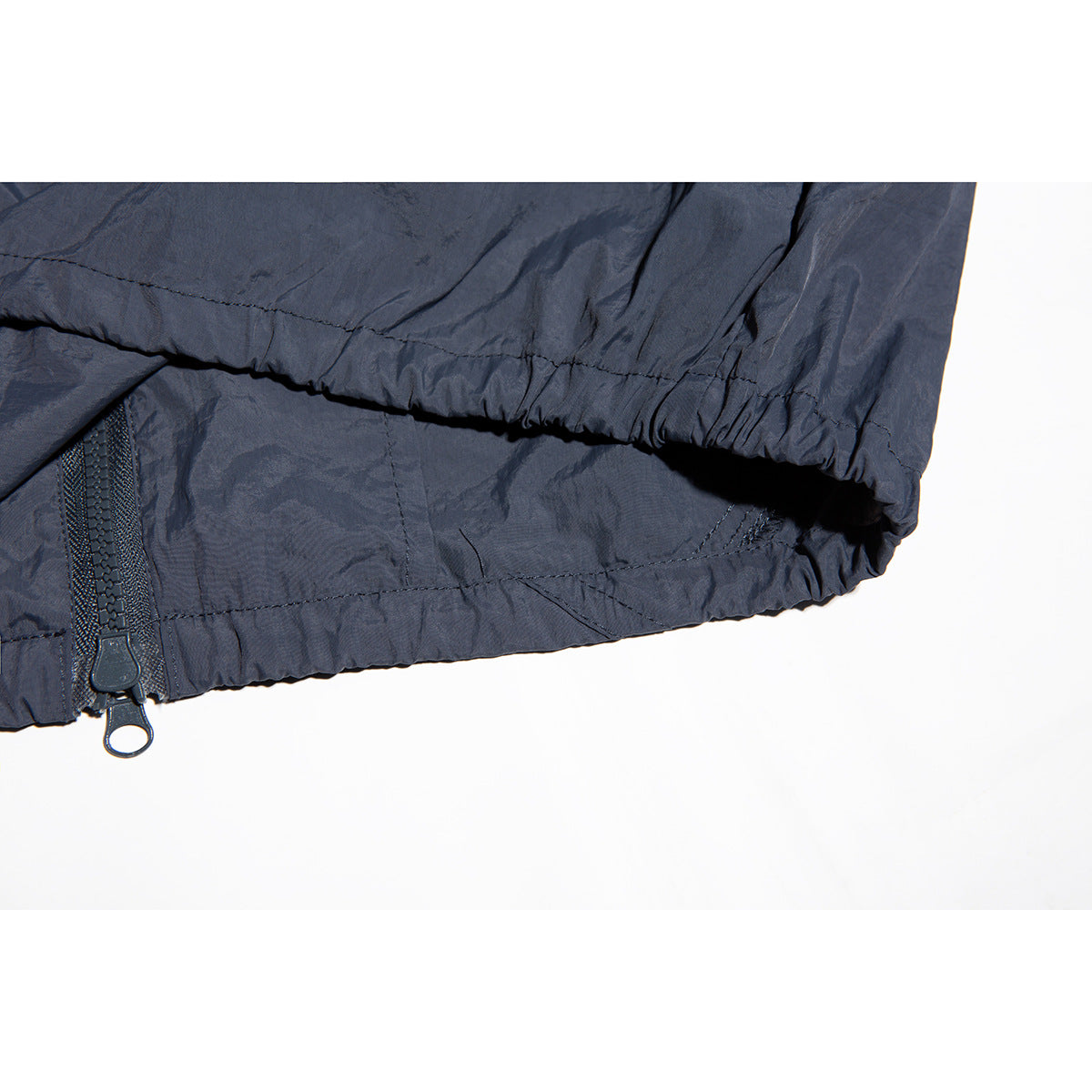 Close-up of the dark navy jacket hem, gathered edge and zipper with two pull tabs.