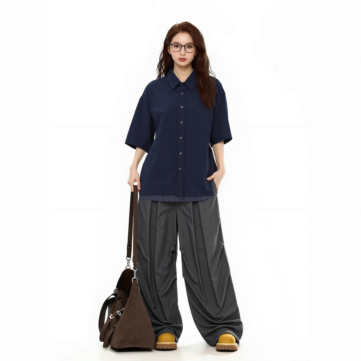Woman facing forward in a navy short-sleeve button-up shirt with a chest pocket and loose gray trousers.