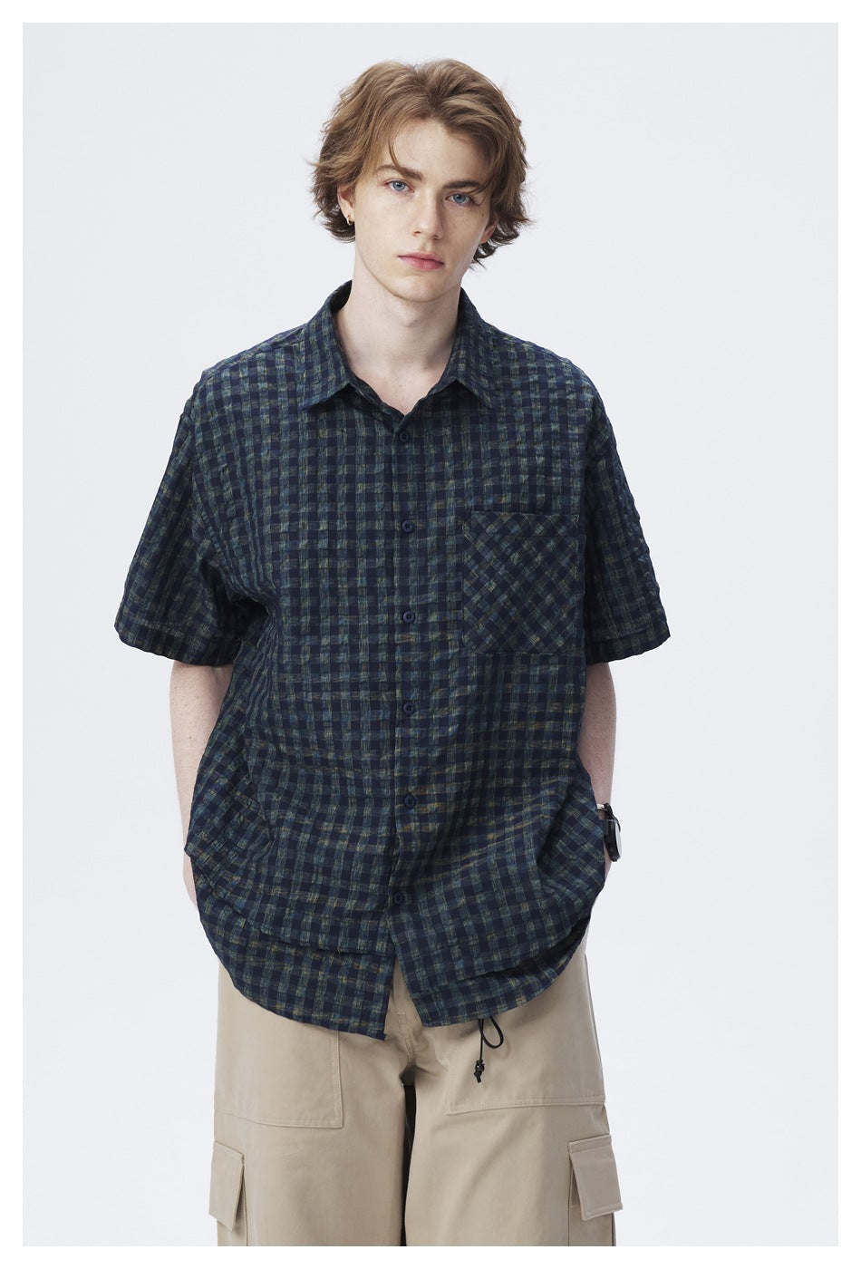 Front view of a model wearing a dark navy and green plaid short-sleeve shirt with a chest pocket.