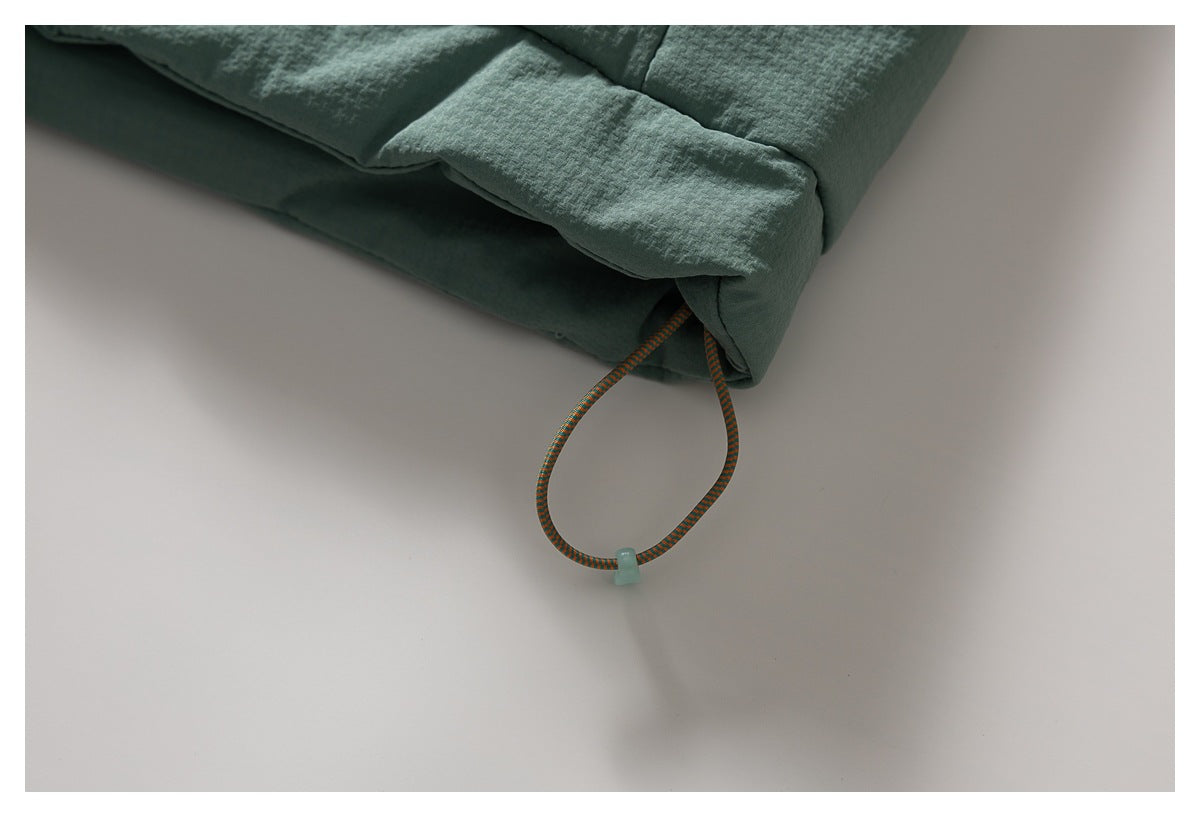 Close-up of a sage green garment hem with a loop of multicolored elastic cord and a small toggle.