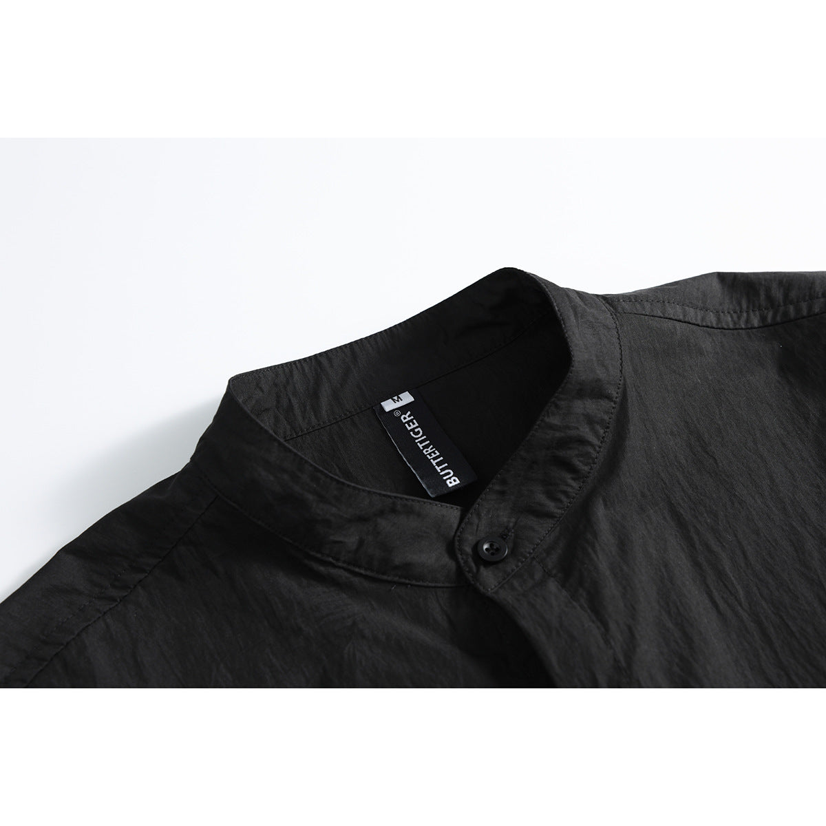 Close-up of a black shirt's stand collar, button, and inner neck label.