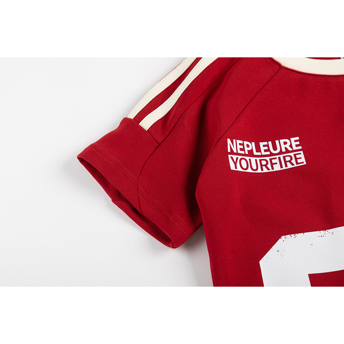Close-up of a red jersey sleeve and chest with cream shoulder stripes and white lettering.