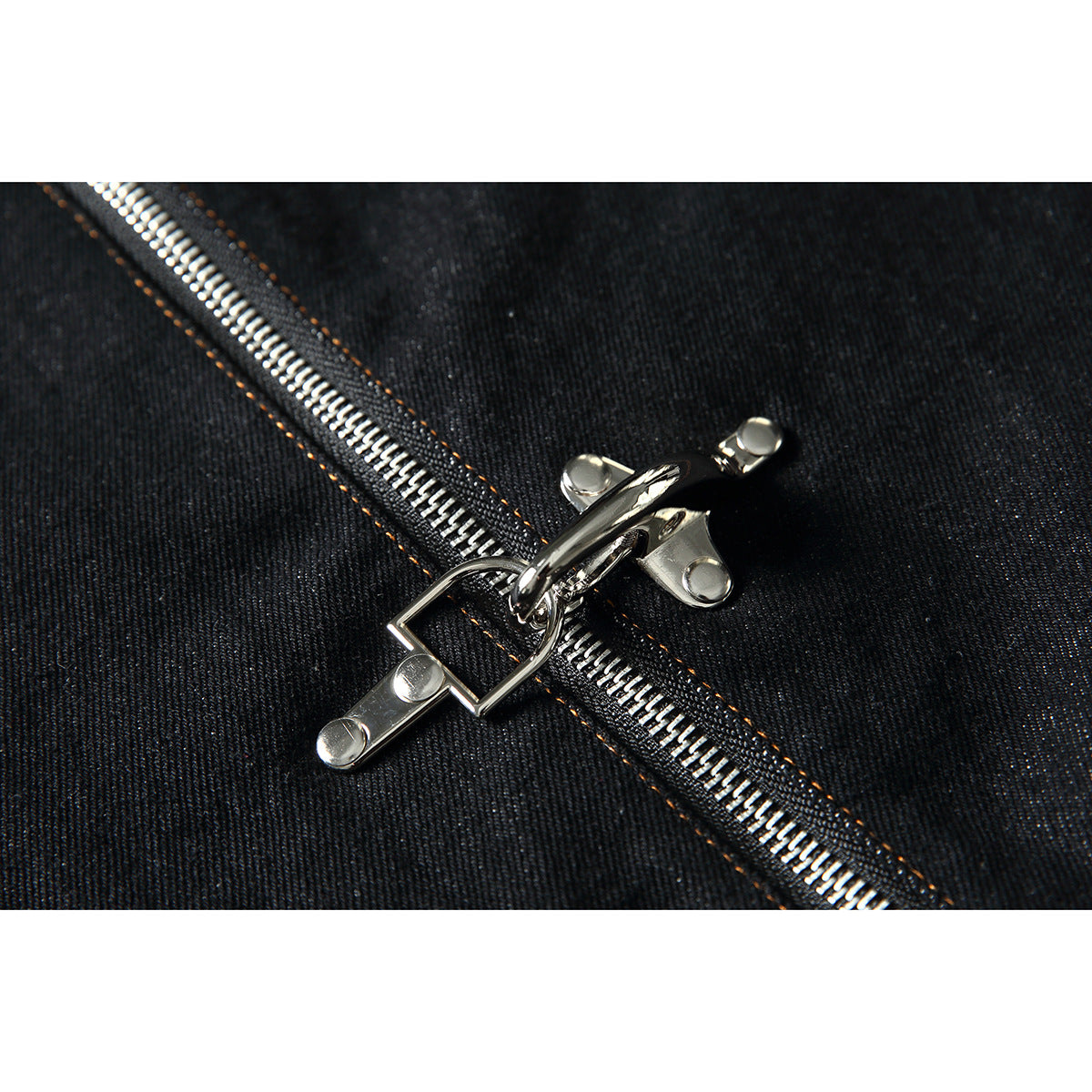 Close-up of a silver double zipper on black denim with orange stitching.