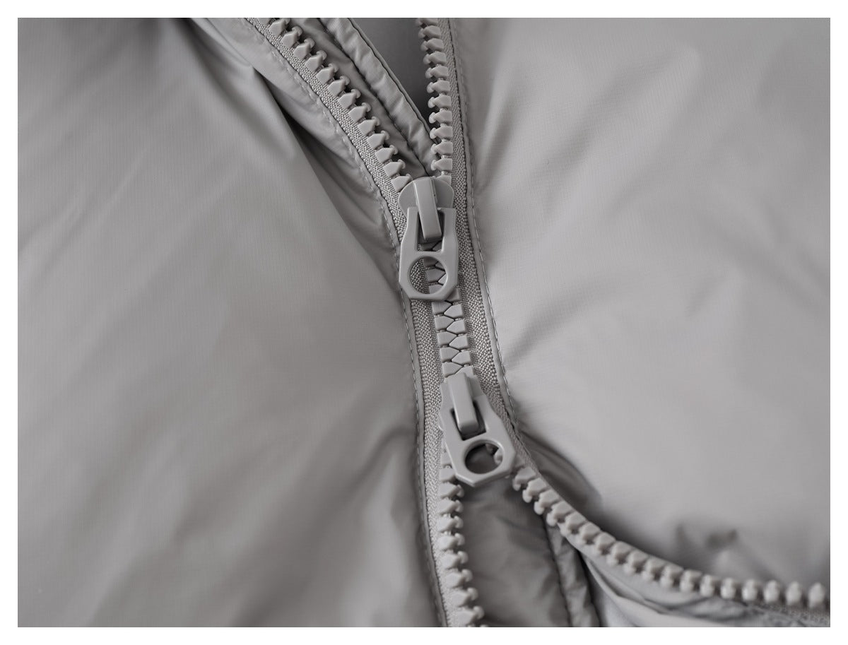 Close-up of two zipper sliders on the front of a gray padded jacket.