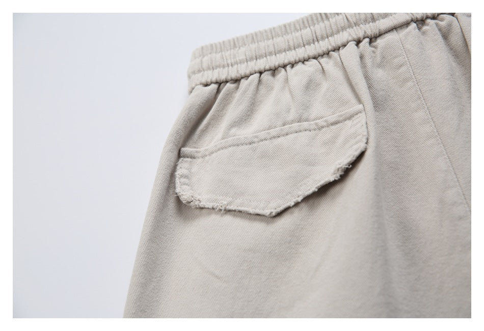 Close-up of a rounded flap pocket and elastic waistband on beige trousers.