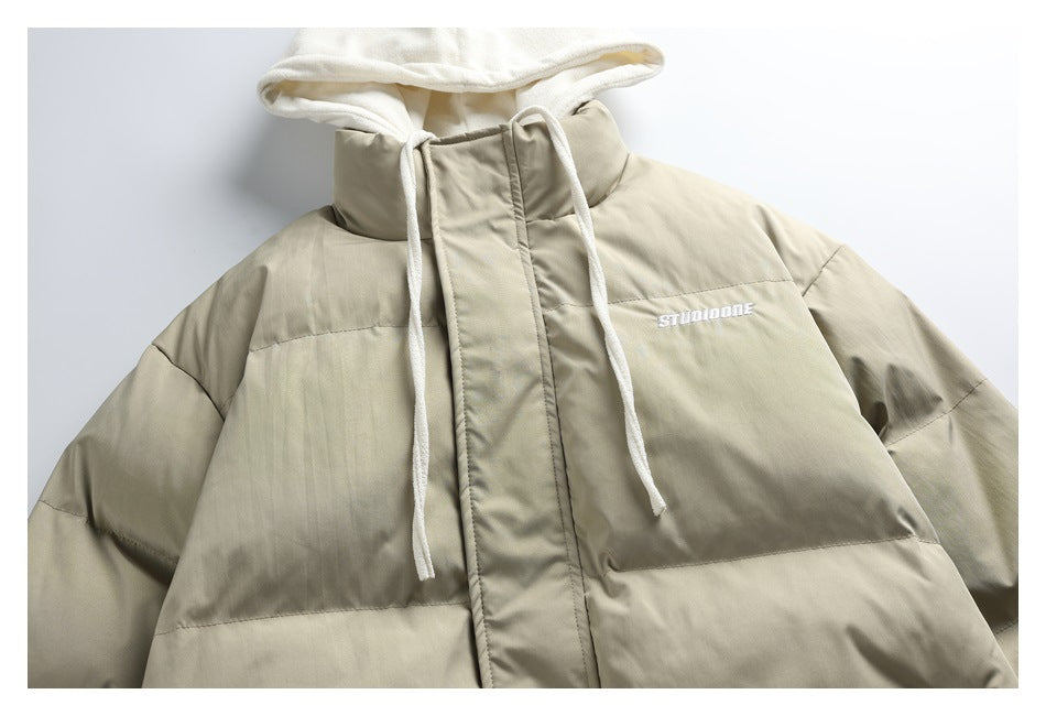 Front close-up of a beige padded jacket with a white hood, long drawstrings and small white chest embroidery.