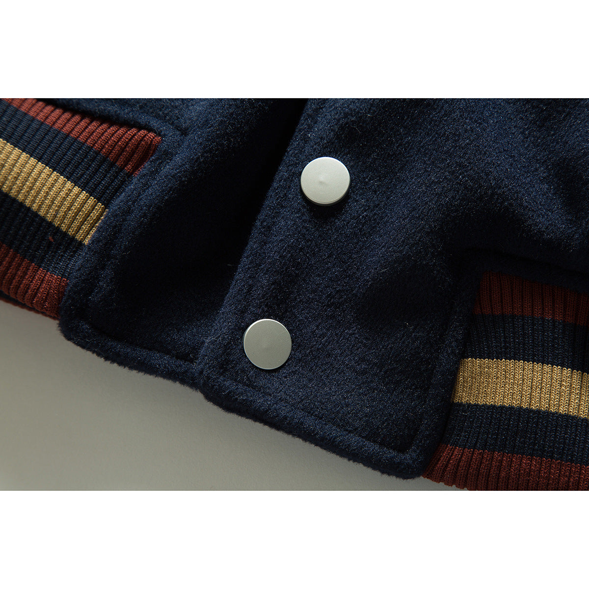 Close-up of a navy jacket front with two pale snaps and striped ribbed cuffs.