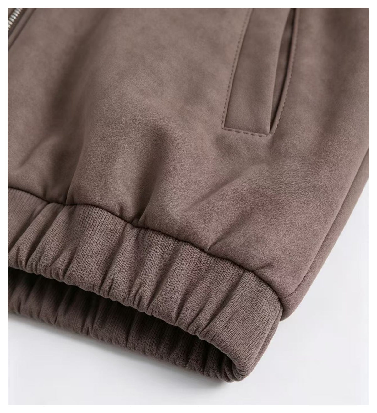 Close-up of a taupe-brown garment showing a slanted pocket opening and a wide ribbed elastic edge.