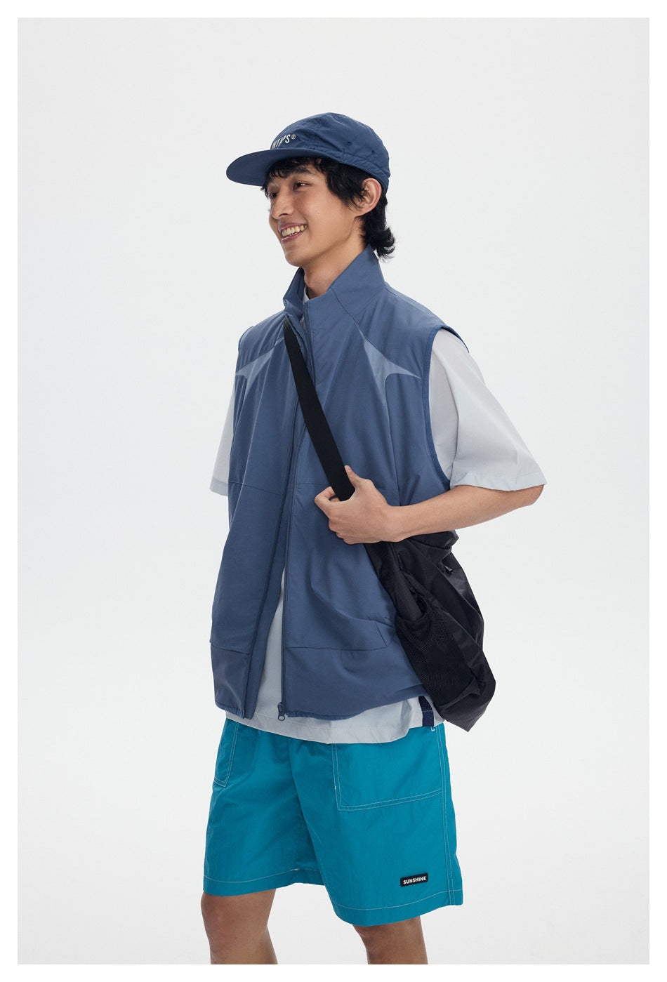 Three-quarter view of a model wearing a blue-gray sleeveless vest, white T-shirt, and turquoise shorts.
