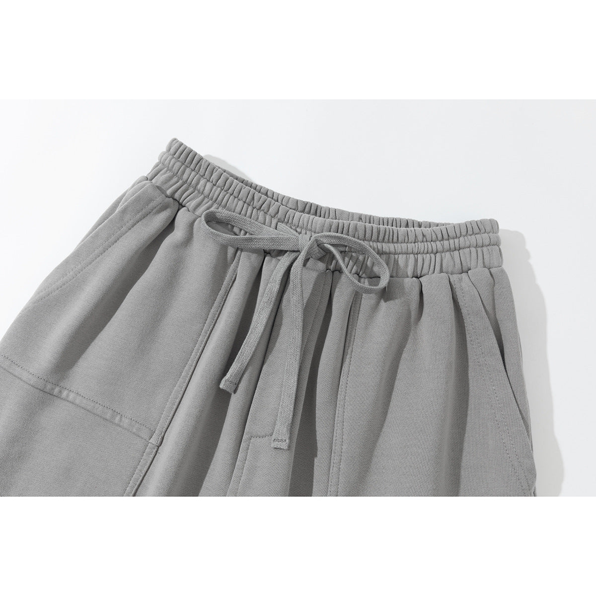Close-up of light gray pants showing the elastic waistband, drawstring, and front pocket.