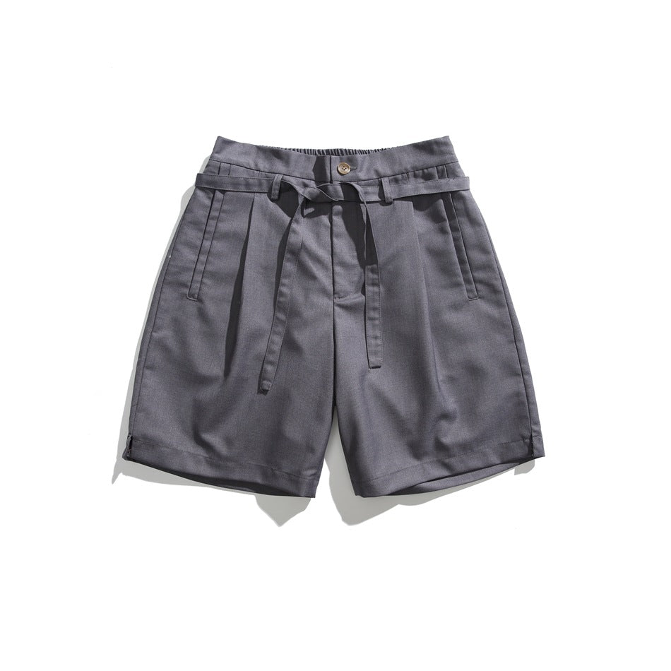 Dark gray pleated knee-length shorts with button, tie belt and slanted front pockets, flat lay
