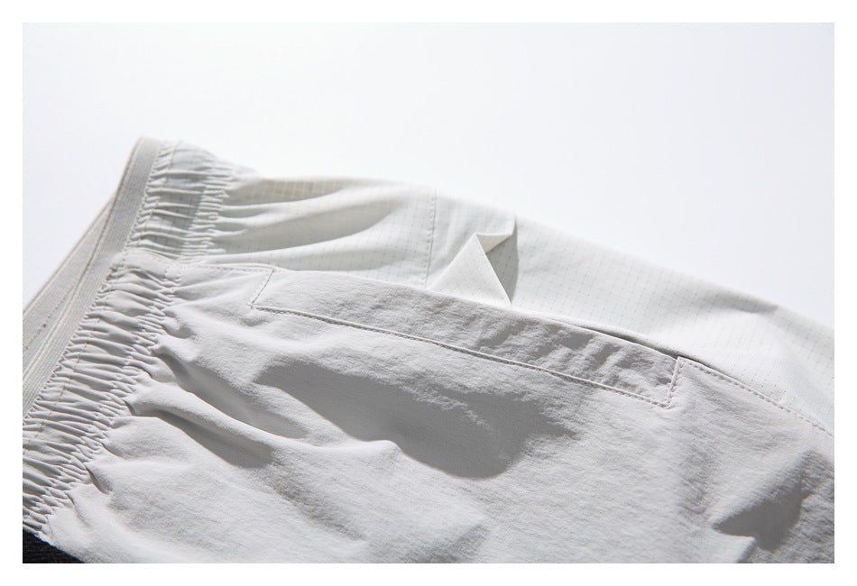 Close-up of a stitched pocket opening and grid-patterned panel on light gray shorts.