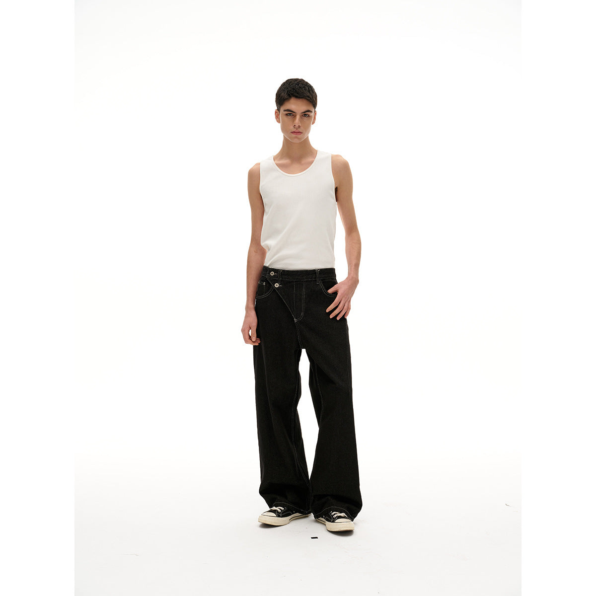 Model wearing a white sleeveless tank top and loose black jeans, standing against a plain white background.