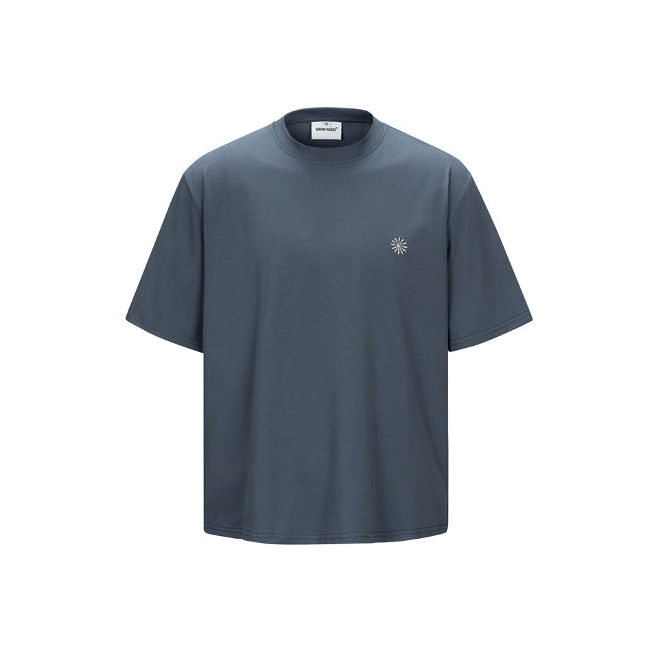 Gray-blue short-sleeve crew-neck T-shirt, front view, with a small light sunburst emblem on the left chest